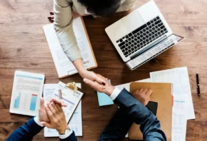 Equipe reunida em uma mesa de escritório analisa relatórios, gráficos e documentos enquanto usa notebook. Contexto de gestão e planejamento com foco em Sustentabilidade nos negócios: Ações simples que geram impacto positivo.