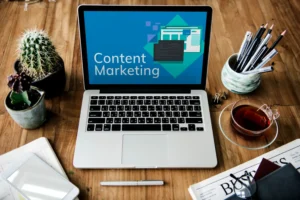 Mesa de trabalho com notebook exibindo “Content Marketing”, ao lado de cactos, canetas e xícara de chá, representando marketing de conteúdo para pequenas empresas e estratégias eficazes.
