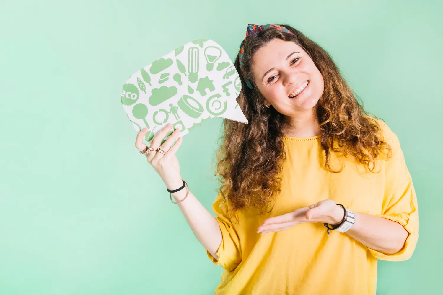 Jovem sorridente segurando um balão de fala com ícones de pensamento em fundo verde, sugerindo tema de Inteligência emocional: Como desenvolver na prática no dia a dia com dicas visuais e foco em autoconhecimento.